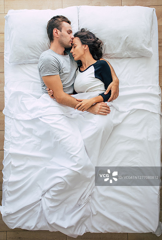 睡觉前。一家人都在睡觉。一对相爱的美丽的年轻夫妇躺在白色的大床上休息。丈夫和妻子一起在床上。俯视图图片素材