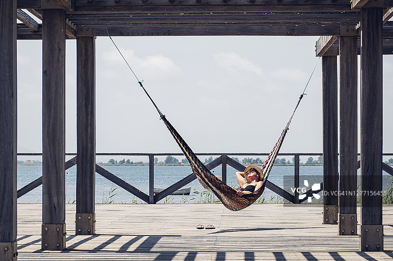 放松的女子躺在吊床上，吊床悬挂在木板路上的金属结构上图片素材