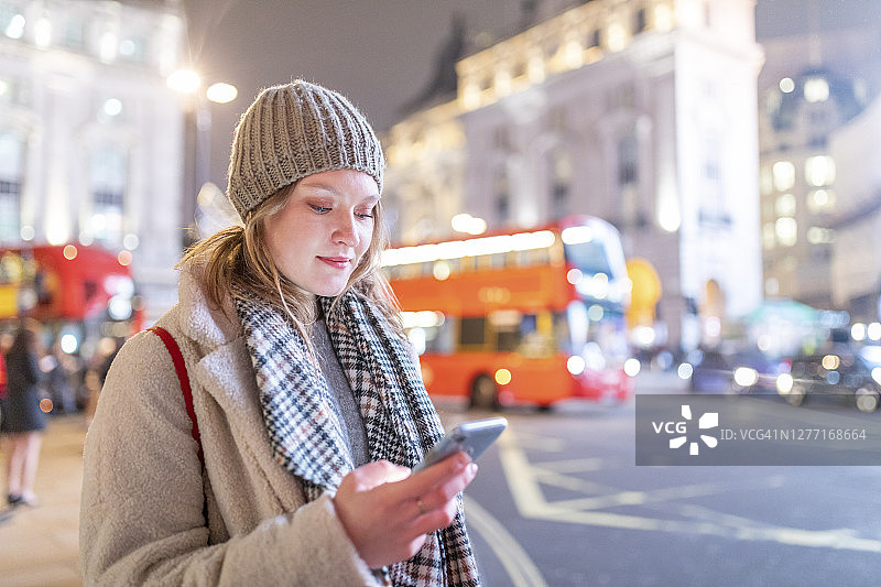 晚上，一名年轻女子站在皮卡迪利广场的街道上使用智能手机图片素材