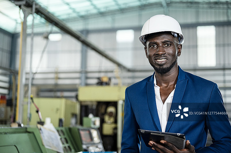 成功的非洲企业家在工厂的信心和使用平板检查生产计划在工厂车间。图片素材