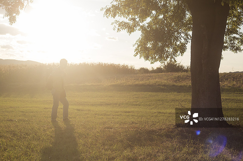在美丽的阳光明媚的日落时分，一名成年男子在乡村徒步旅行图片素材