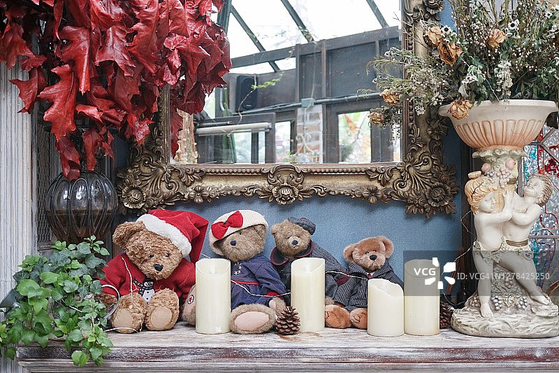 泰迪熊。坐在一起的泰迪熊毛绒玩具和壁炉上的蜡烛一起作为装饰。复古的设置与窗户灯。图片素材