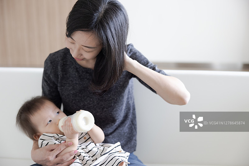可爱的亚洲宝宝喜欢妈妈膝上的奶瓶图片素材