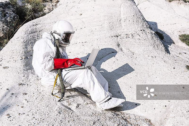 男宇航员坐在山上用笔记本电脑工作图片素材