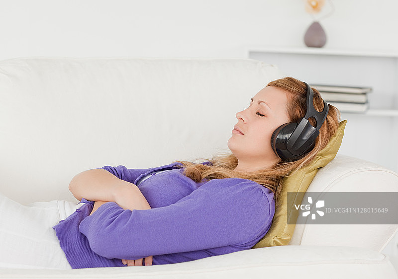 漂亮的红发女人听着音乐，躺在沙发上休息图片素材