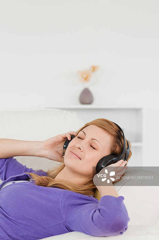 美丽的红发女子一边听音乐，一边躺在沙发上休息图片素材