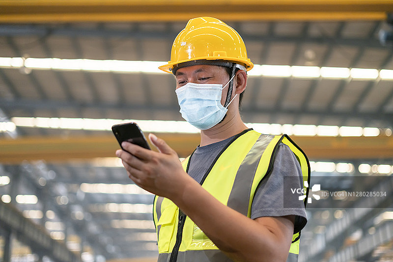 在工厂里，一名戴着口罩的男工人正在看手机图片素材