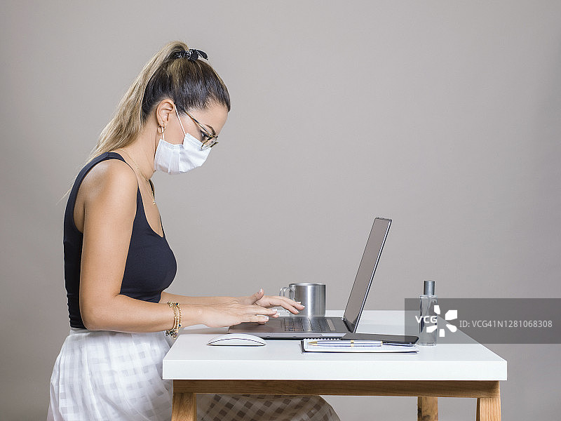 戴着口罩在办公室用笔记本电脑工作的女商人图片素材