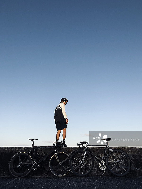 一个骑自行车的年轻人和他的自行车站在海滩附近的天空。图片素材