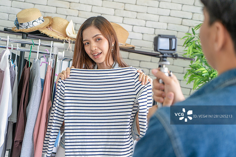 年轻美女视频博主通过智能手机上的技术在社交媒体上直播卖衣服。高加索部落客正在录下病毒式的片段并在流媒体互联网上分享。图片素材
