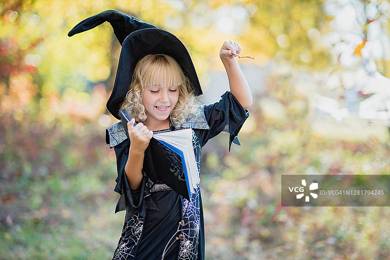 穿着女巫服装的小女孩在户外庆祝万圣节，玩得很开心。图片素材