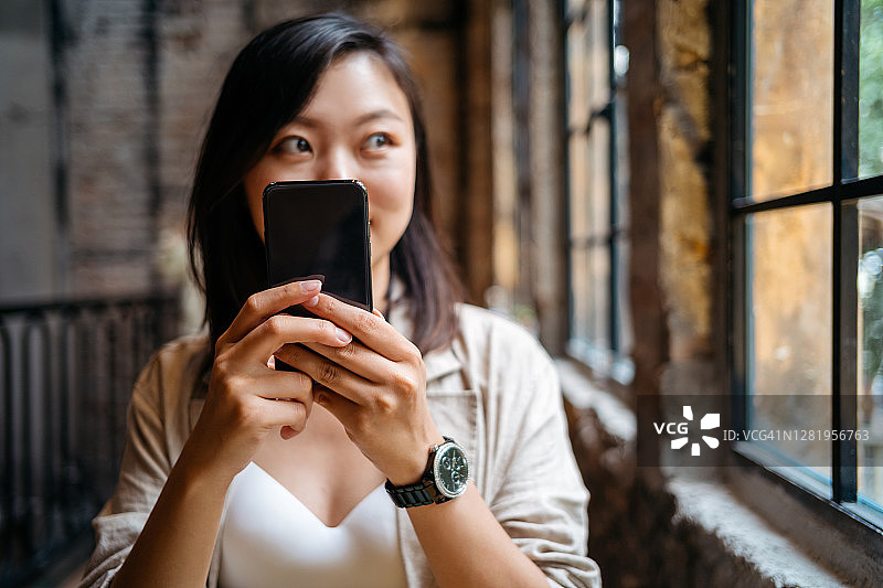 微笑的年轻亚洲女子在咖啡馆使用智能手机图片素材