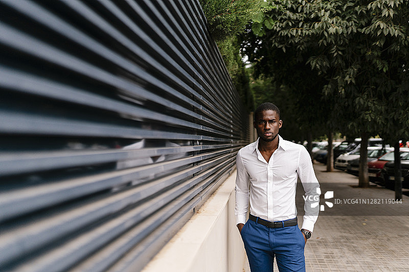 自信的非洲专业人士双手插在口袋里站在城市的围墙旁图片素材