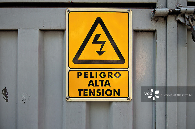 金属门上的西班牙语警告标志上写着“Peligro: alta tensión”(危险:高电压)图片素材