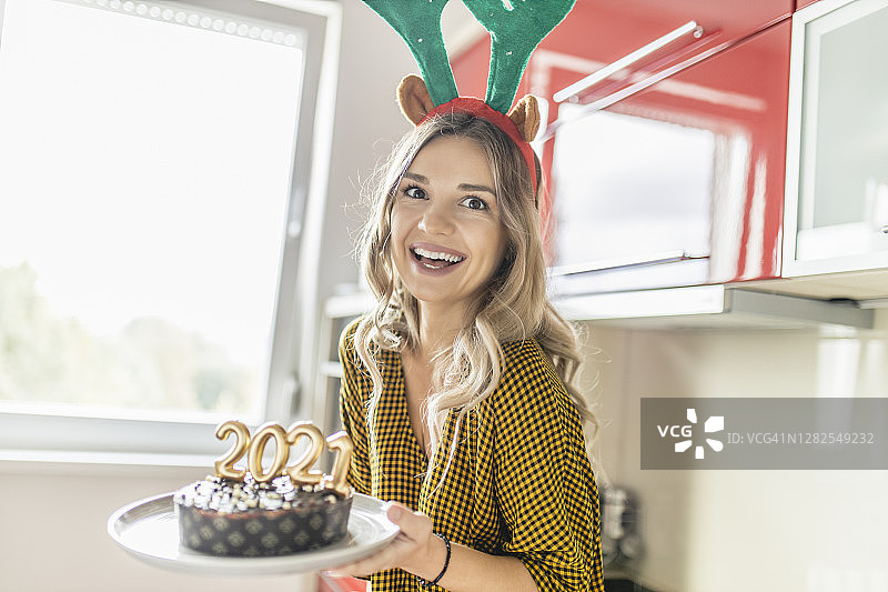 一名年轻女子正在制作并装饰巧克力蛋糕，蛋糕上点燃蜡烛，形状为2021年新年派对的数字图片素材