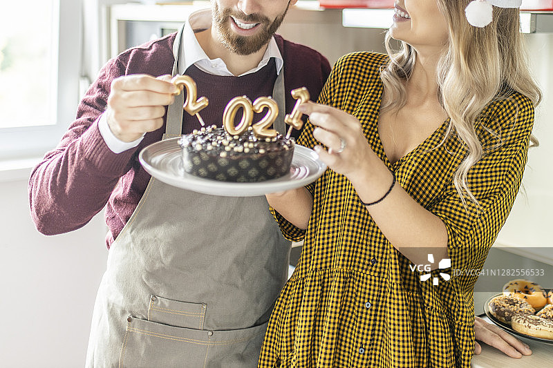 这是一对年轻夫妇在家里用点燃的蜡烛制作和装饰巧克力蛋糕的特写图片素材