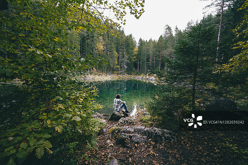 一个人坐在森林里欣赏着翠绿的湖水图片素材