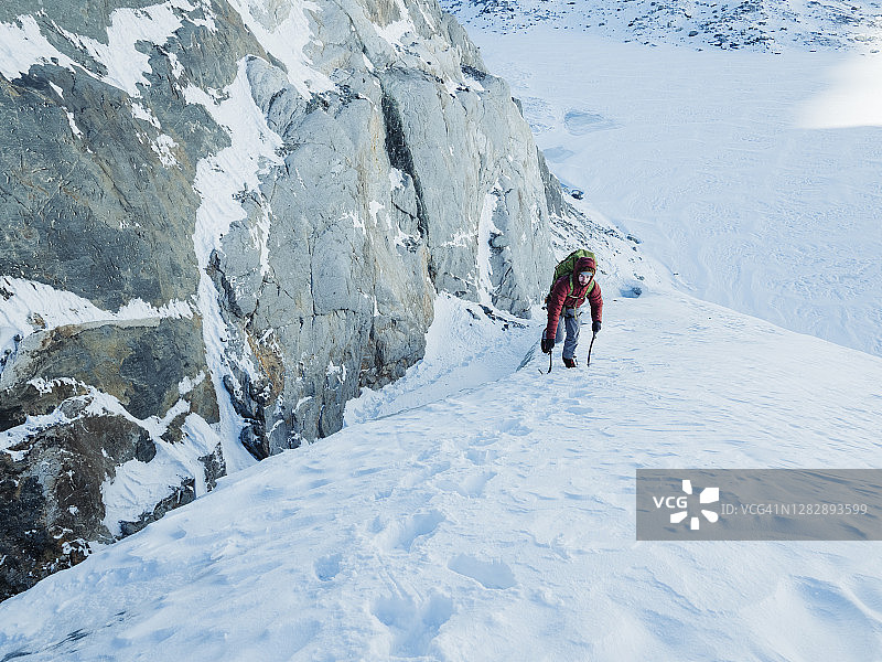 一个冰上攀登者手拿两把冰斧爬上冰川上陡峭的雪坡图片素材