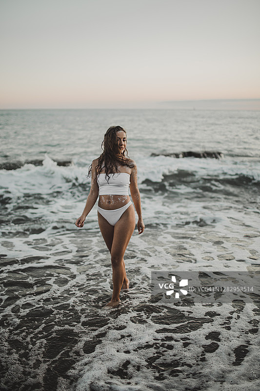 晒黑的性感女孩在亮片站在水的海滩上浪花飞溅图片素材