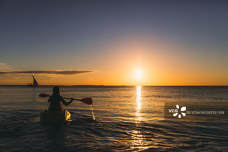 一名年轻女子在桑给巴尔岛美丽的日落中划着皮艇图片素材