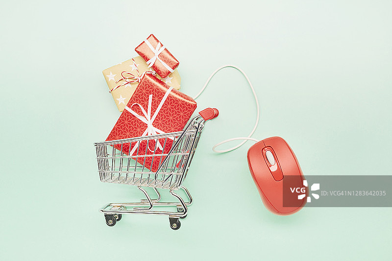 高角度的小购物车，圣诞礼物和红色电脑鼠标在绿松石色的背景，网上购物图片素材