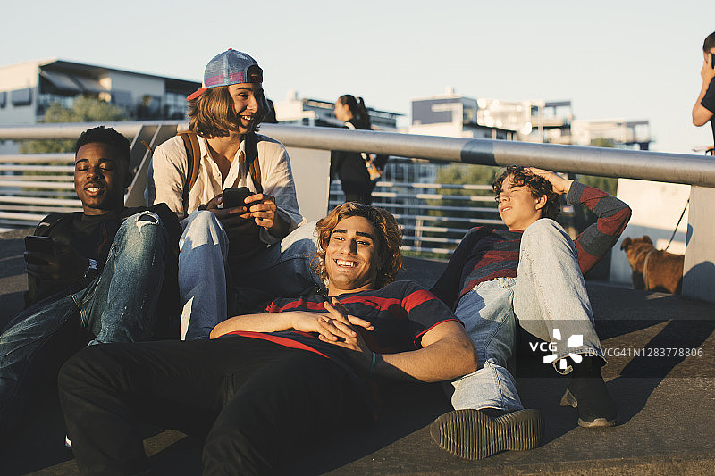 微笑的年轻和十几岁的男性朋友享受着躺在城市图片素材