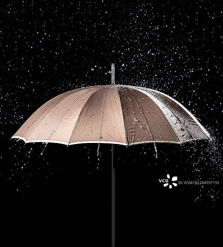 打开的伞上有雨滴从天空中落下在黑色的背景上。图片素材