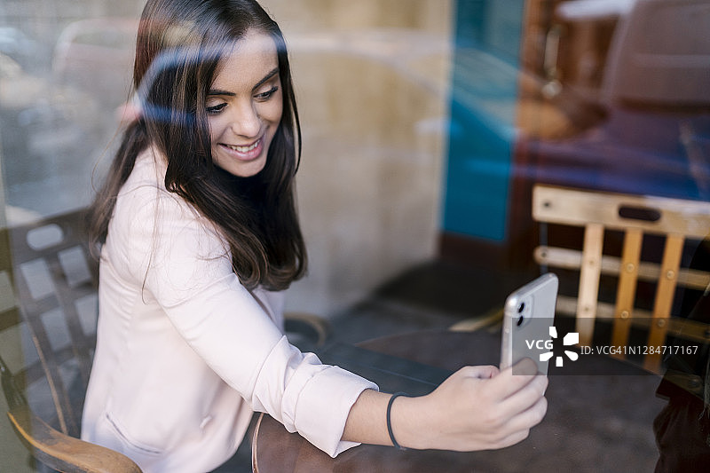 微笑的年轻女企业家在咖啡馆用智能手机自拍图片素材
