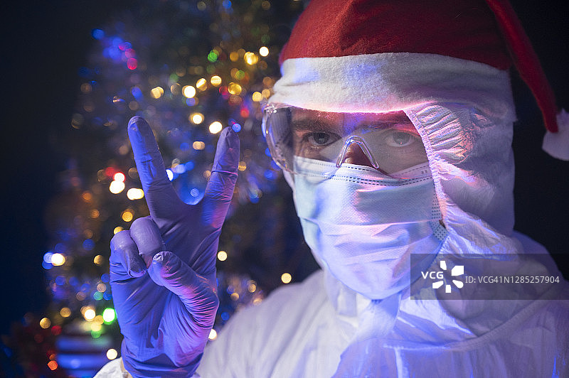 科学家和圣诞老人做胜利手势。有一棵装饰过的圣诞树，背景上有灯光。图片素材