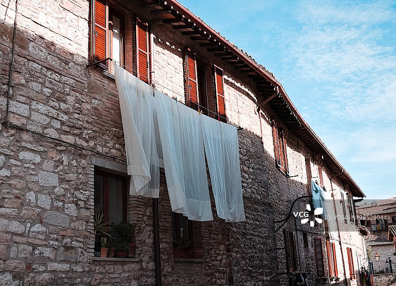 中世纪意大利村庄古比奥(古比奥，翁布里亚，意大利，欧洲)一幢古老的石头房子的窗户外晾着床单图片素材