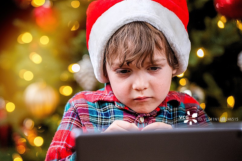 悲伤的小男孩戴着圣诞老人的帽子用电子平板电脑和他的祖父母聊天图片素材
