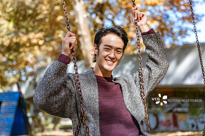 一个快乐的日本年轻人在秋千上的肖像图片素材