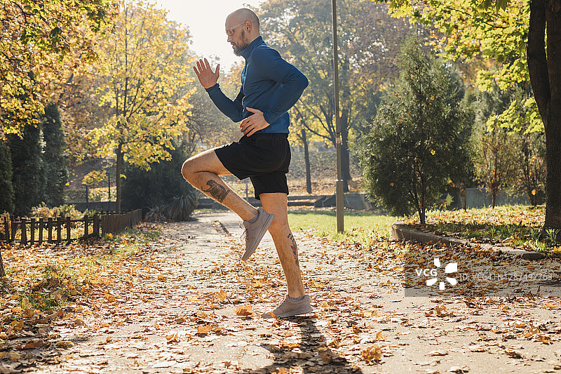 一位戴着墨镜的健美白人男子在公园跑步前热身的侧视图(秋季)图片素材