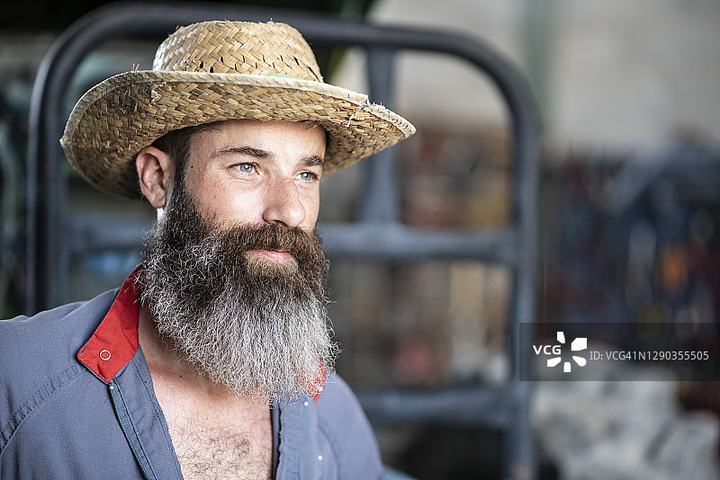 在仓库里戴着帽子穿着工作服的大胡子工人的肖像图片素材