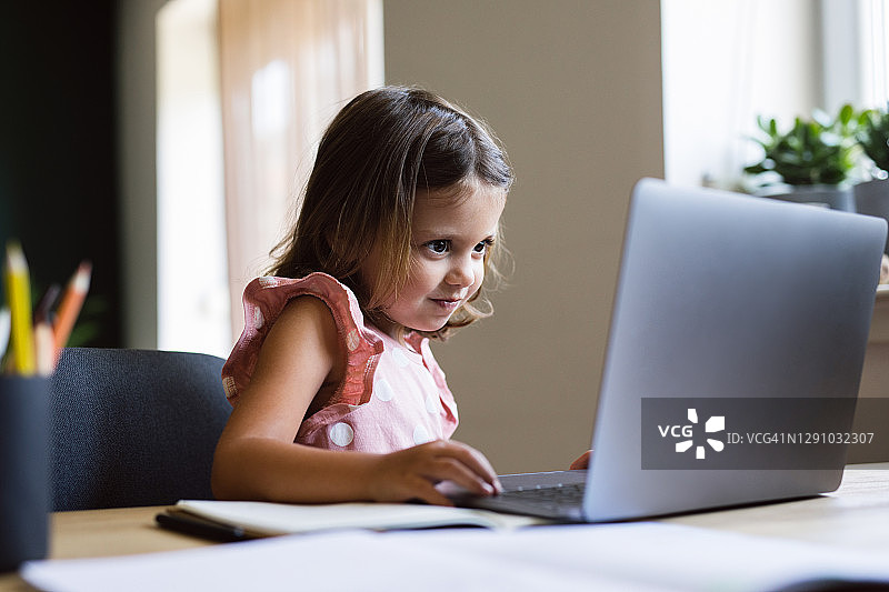 快乐的年轻女孩在家里的客厅里使用笔记本电脑图片素材