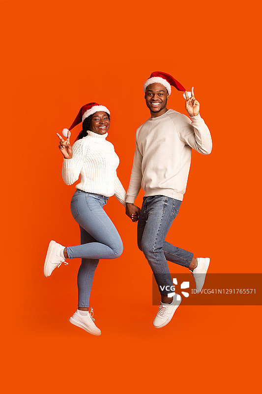 顽皮的黑人夫妇戴着圣诞老人帽，手牵着手，摆出和平的姿态图片素材
