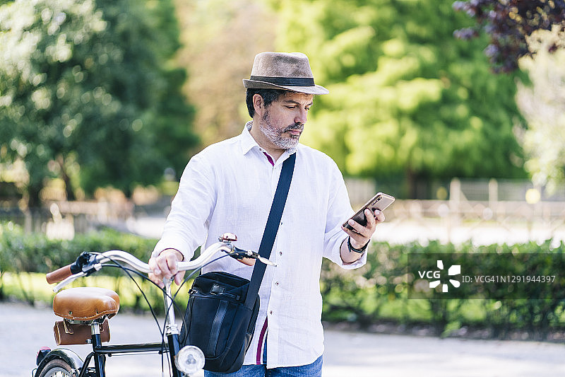 一个成熟的男人在公园里用手机和自行车站在一起图片素材