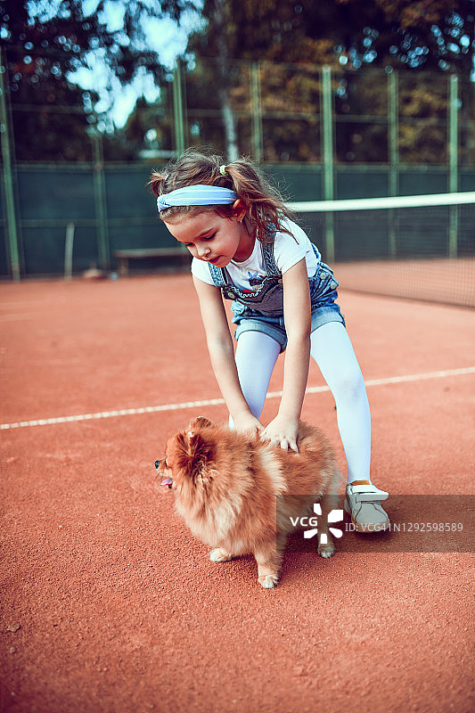 可爱的小女孩在网球场上和狗玩图片素材