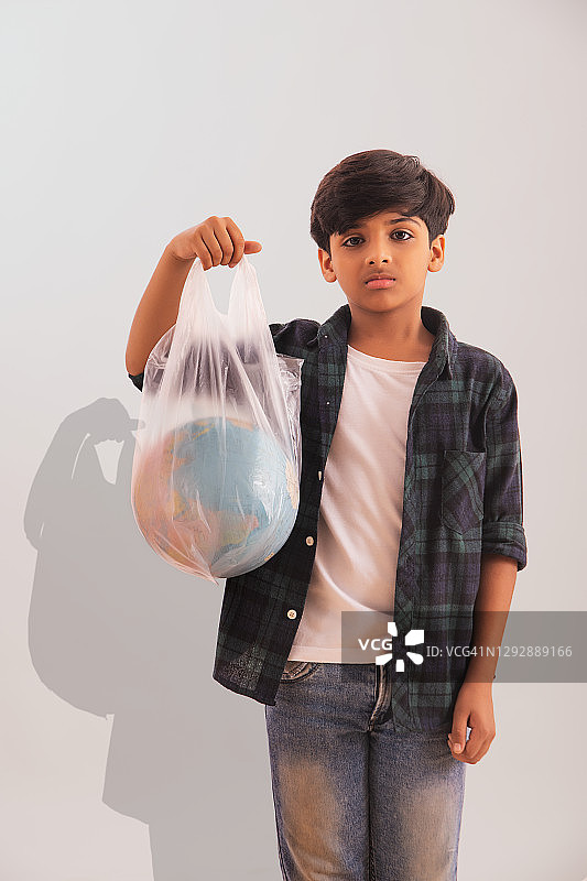 一个小男孩拿着一个装在塑料袋里的地球球，传递一个关于环境的信息。(儿童)图片素材