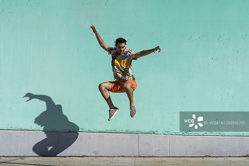 休闲男子跳在彩色墙前图片素材