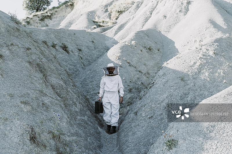 一个带着公文包穿着养蜂人衣服的人在一个干燥的世界末日景观中图片素材