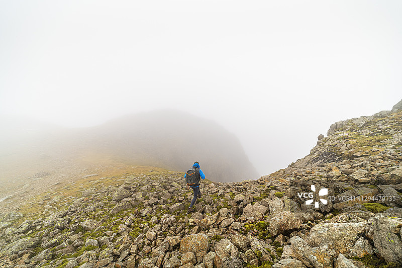 在湖区国家公园浓雾中，一名男子在布满岩石的峭壁顶峰徒步旅行图片素材