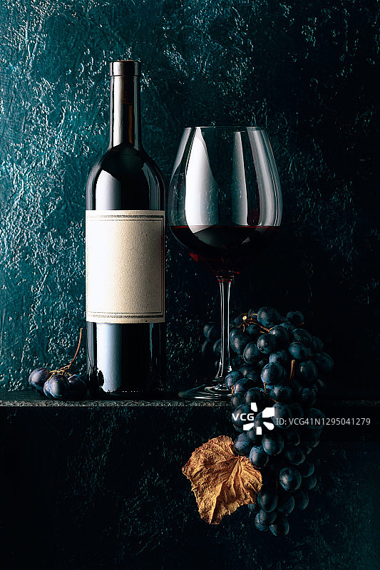红酒和蓝色的葡萄与干燥的藤叶在一个古老的深蓝色背景。图片素材