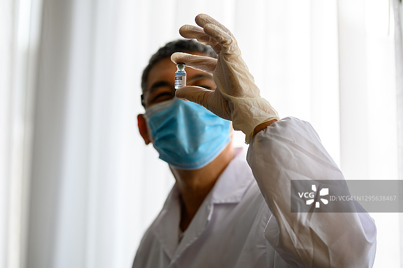 一位亚洲科学家戴着医用手套在实验室里拿着小瓶剂量的冠状病毒疫苗图片素材