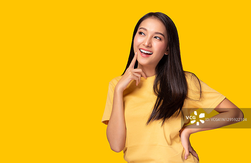 肖像年轻的亚洲女人看拷贝空间漂亮的女孩穿黄色T恤与黄色的背景在工作室漂亮的亚洲女性得到自信。女人得到满足的东西可爱的女人得到快乐图片素材