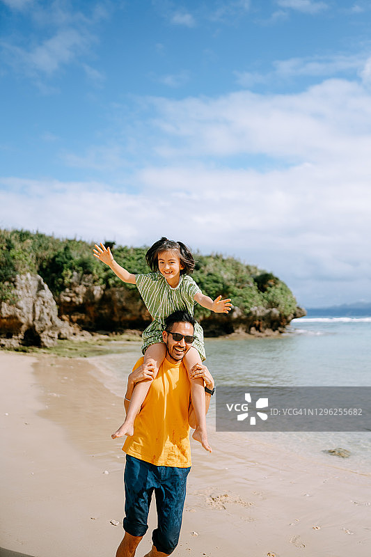 父亲背着激动的女儿在沙滩上跑步图片素材