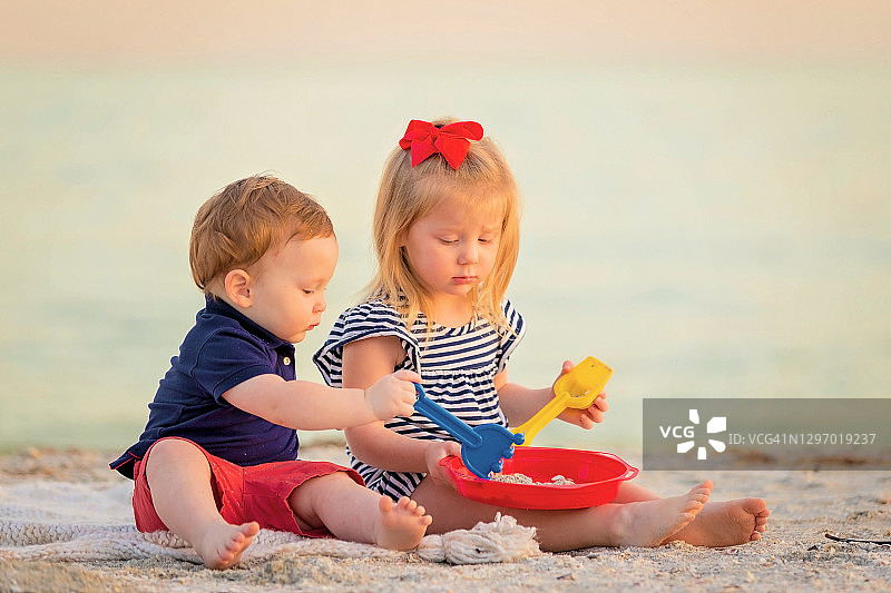 小弟弟和小妹妹坐在沙滩上玩玩具图片素材