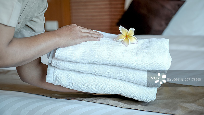 酒店服务员的手把鸡蛋花和毛巾放在豪华酒店房间的床上，为游客旅游做好准备图片素材