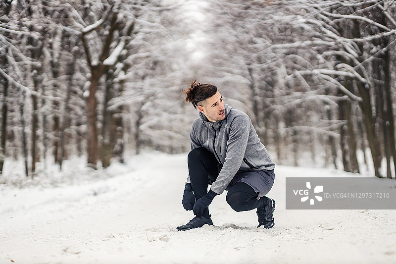 雪天的森林里，运动员跪着系鞋带。运动服装，健康生活方式，冬季健身图片素材