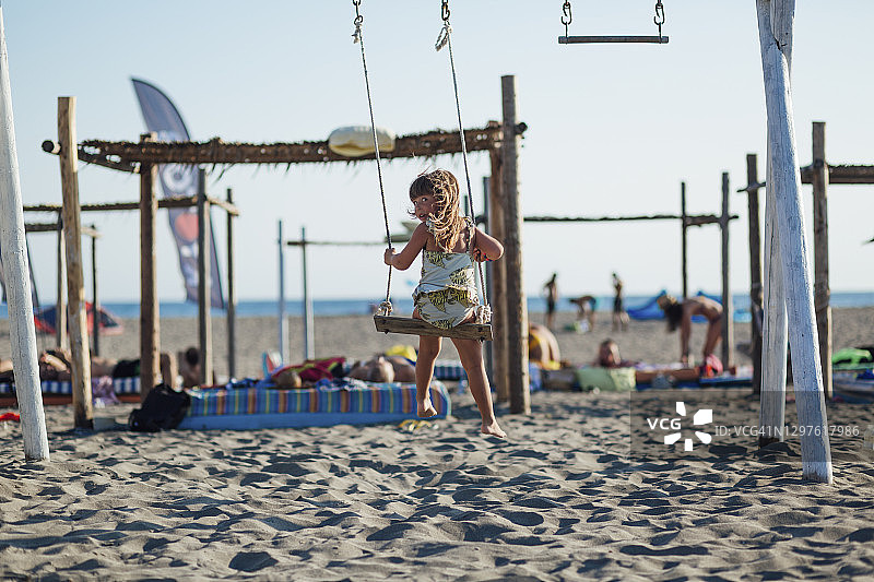 一个美丽的白人小女孩在海滩上荡秋千的后视图图片素材